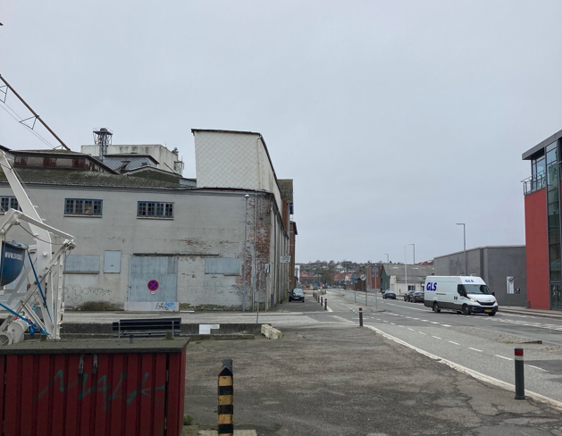 Hvid industribygning med en vej til højre, hvorpå der kører en varevogn